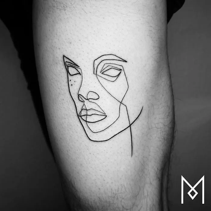 Single continuous line tattoo by Mo Ganji, featuring a minimalist face design on skin.