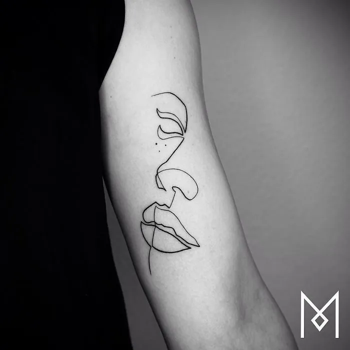 Single continuous line tattoo of a face on an arm by Mo Ganji.