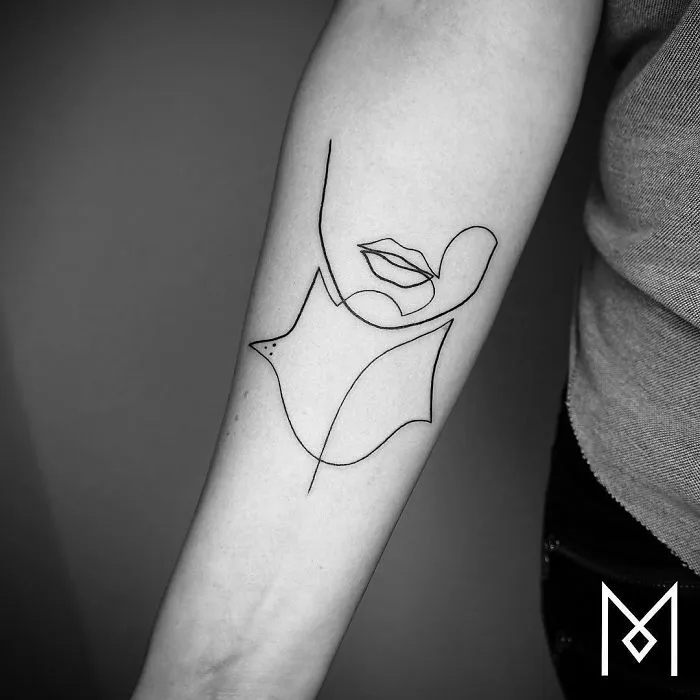 Continuous line tattoo of a face and leaf on an arm by Mo Ganji.