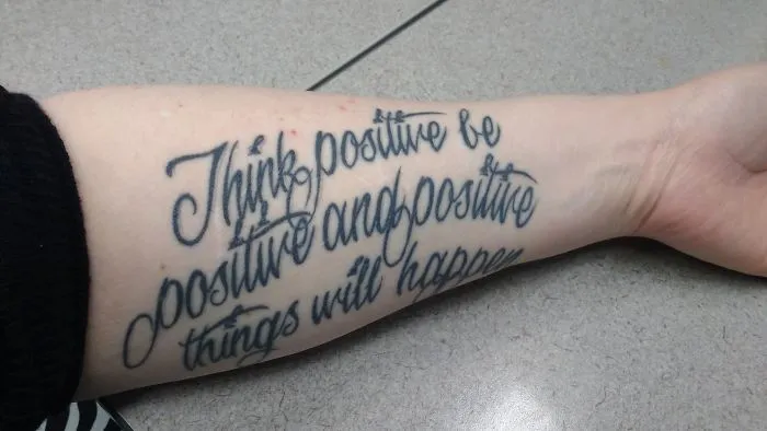 Tattoo covering scar with inspirational text on an arm, transforming it into art.