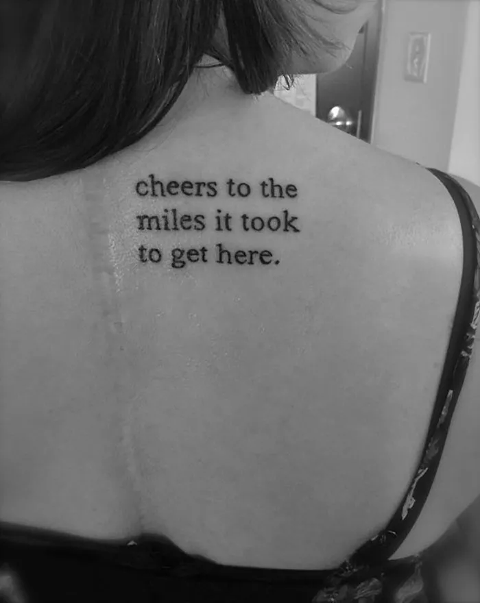 Tattoo art on a back with the text "cheers to the miles it took to get here," creatively covering a scar.