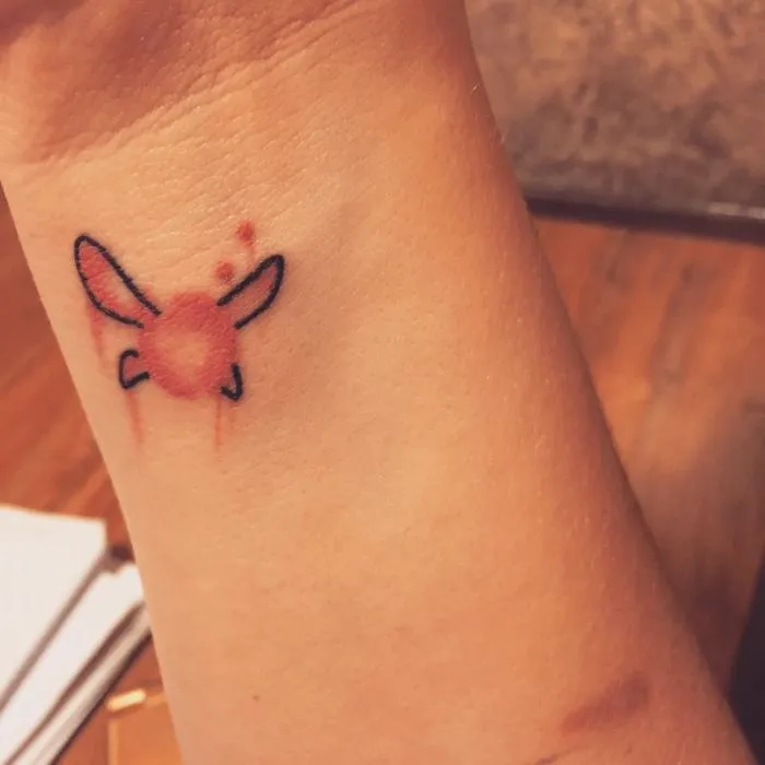 Tattoo transforming a scar on a wrist into a bright, artistic design, featuring a stylized insect.