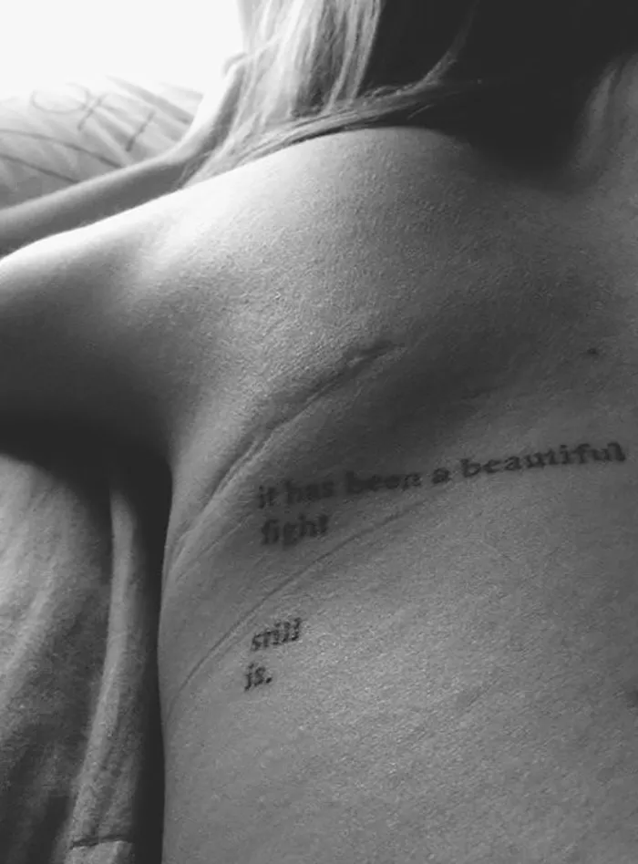 Tattoo words "it has been a beautiful fight" and "still is" above a scar, transforming it into art.