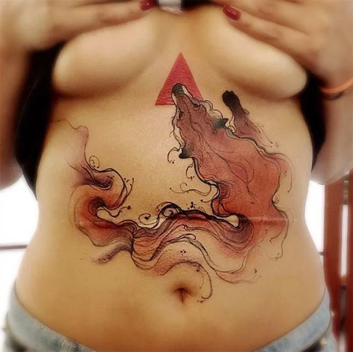 Tattoo art transforming a scar on a person's torso, featuring abstract shapes and a red triangle, creating a striking design.
