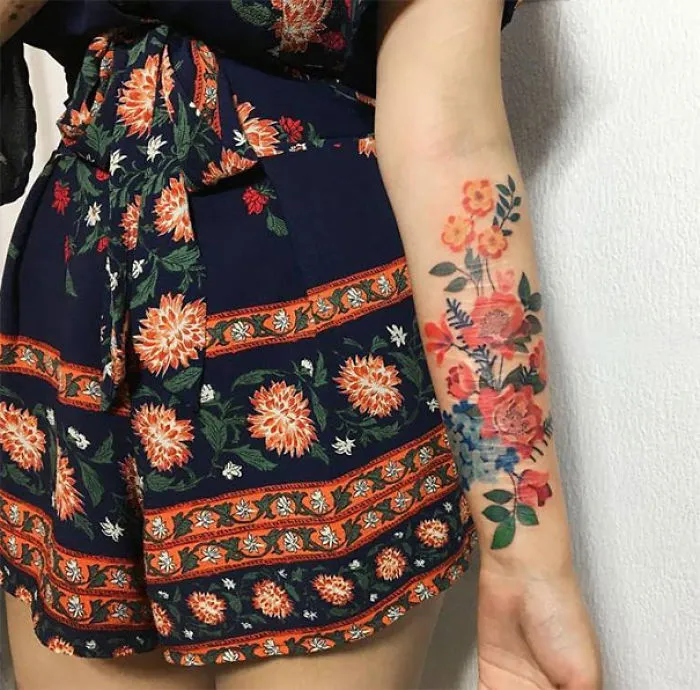 Floral tattoo on forearm creatively transforming a scar into art, paired with a colorful floral dress.