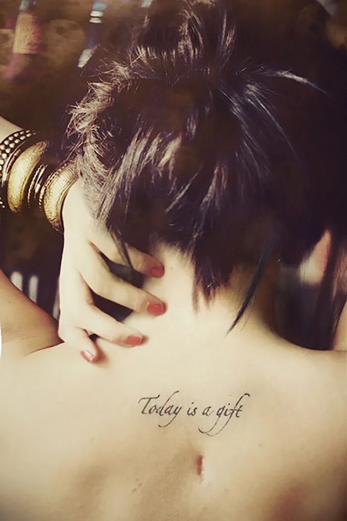 Tattooed quote on a woman's back turning a scar into art.