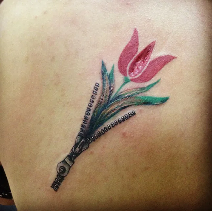 Floral tattoo transforming a scar into art, featuring a zipper opening to reveal a vibrant pink tulip.