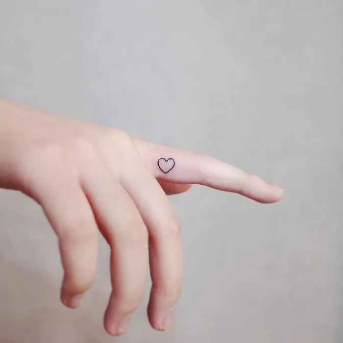 Minimalistic tiny heart tattoo on a finger, representing discreet tattoo style.
