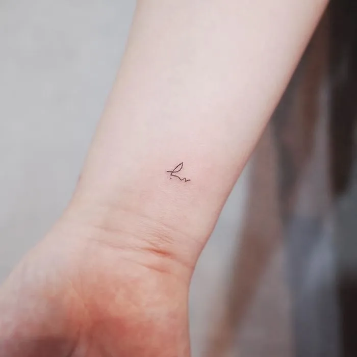 Minimalist tiny tattoo of abstract line art on wrist.