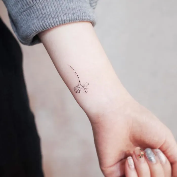 Minimalist tiny flower tattoo on inner forearm of a person in a gray sleeve.