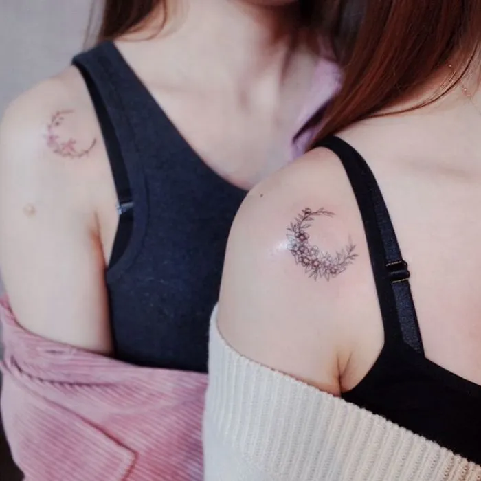 Minimalist crescent moon tattoos on shoulders of two women, showcasing tiny discreet tattoo art.