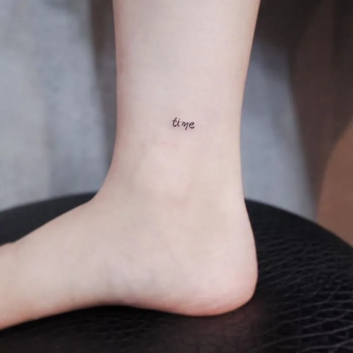 Minimalist tiny tattoo of the word "time" on the lower leg.
