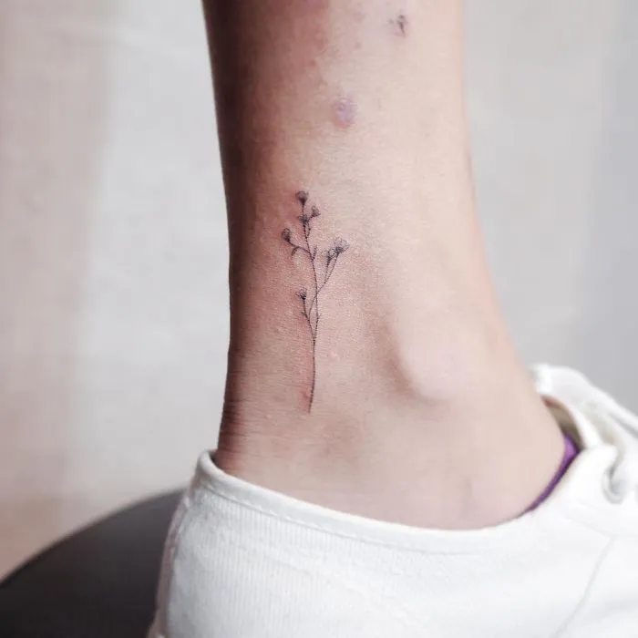 Minimalist tiny tattoo of delicate floral design on ankle.