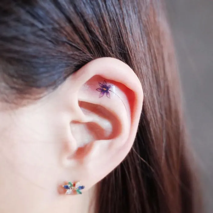 Minimalism tattoo of a tiny flower inside the ear, showcasing discreet design.