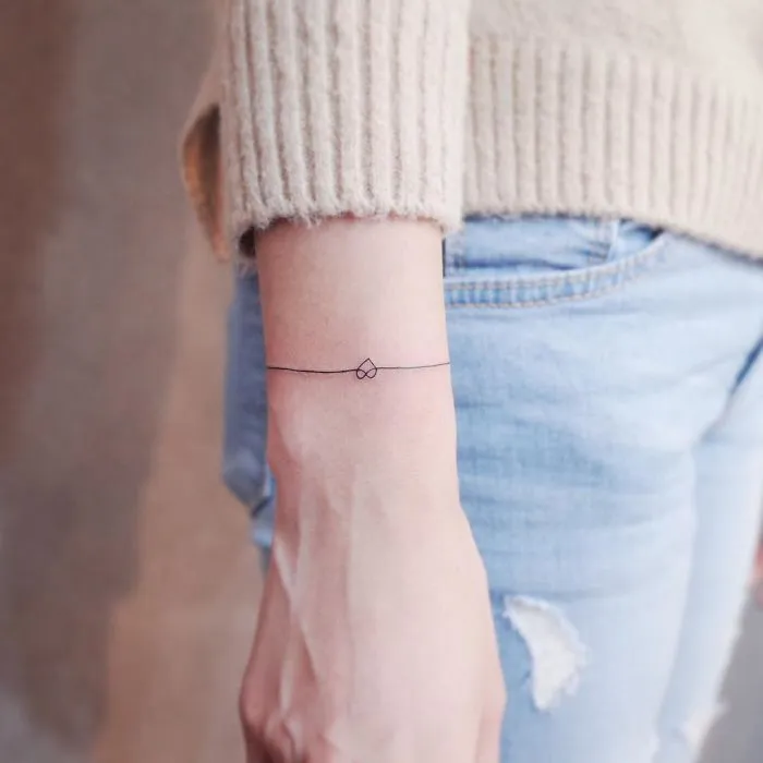 Minimalism tattoo of a heart and line on a person's wrist, showcasing a tiny discreet design.