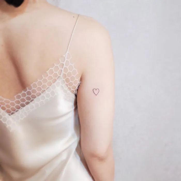 Minimalist tiny heart tattoo on a woman's upper arm, perfect for those who love discreet tattoos and minimalism.
