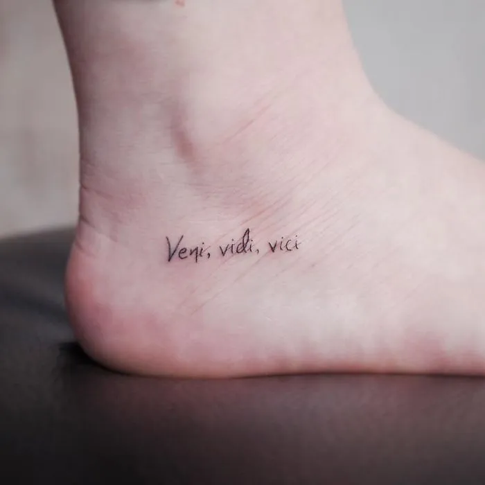 Minimalism tattoo on ankle with the words "Veni, vidi, vici," showcasing a tiny discreet design.