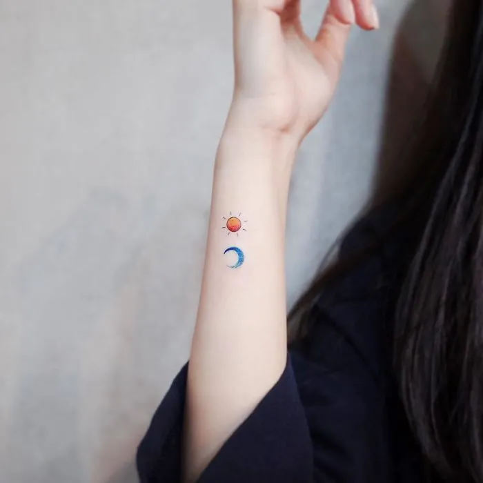 Minimalist tiny sun and moon tattoos on a person's forearm.