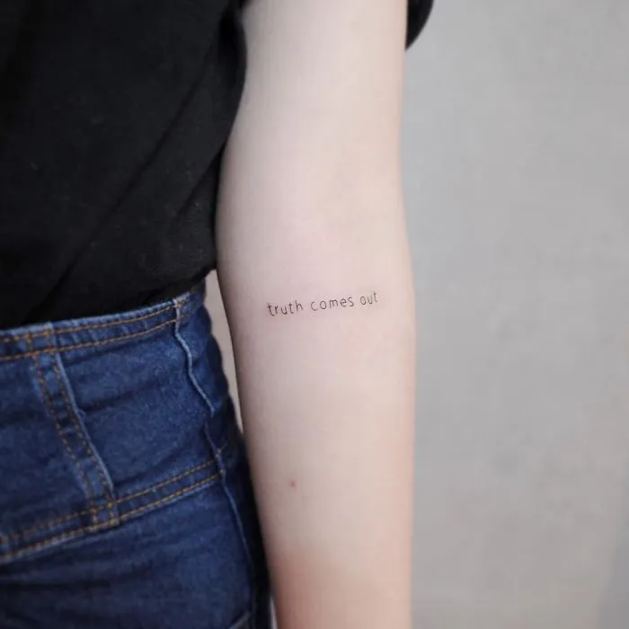 Minimalist tattoo on forearm reads "truth comes out," showcasing discreet body art style.