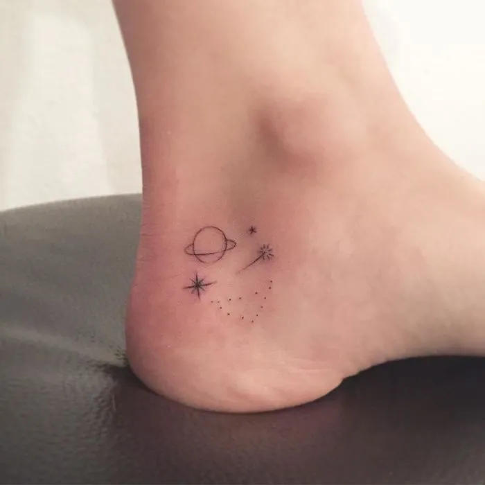 Minimalism tattoo on ankle featuring tiny planetary design and star motifs.