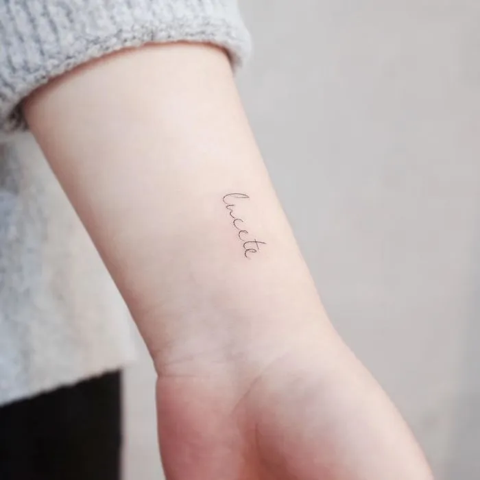 Minimalist tiny tattoo on a person's inner forearm, showcasing the word "lucete" in elegant script.