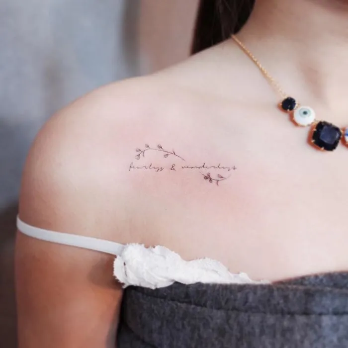 Minimalist tattoo on a woman's shoulder with delicate floral design and text, showcasing discreet tattoo art.