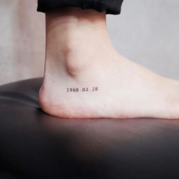 Minimalism-inspired tiny discreet tattoo on ankle displaying numbers.