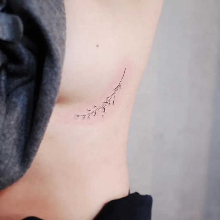 Minimalist tattoo of delicate branches on a person's ribcage, showcasing tiny discreet ink design.