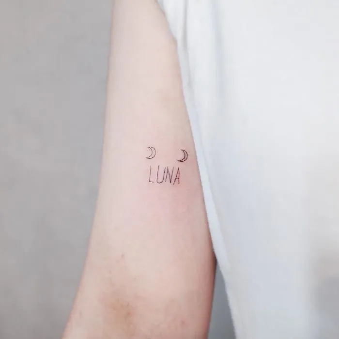 Minimalist tattoo with the word "Luna" and small crescent moons on a person's inner arm.