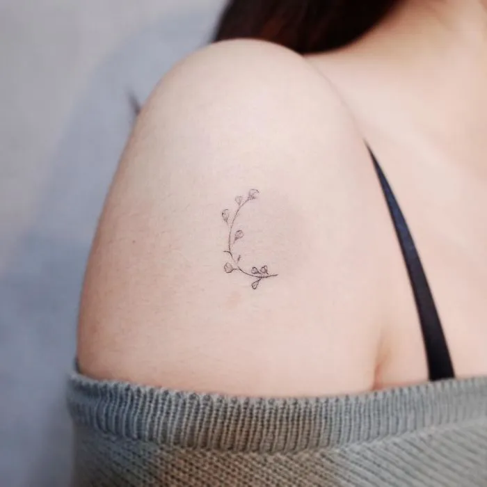 Minimalist tattoo of a delicate branch on a person's shoulder.