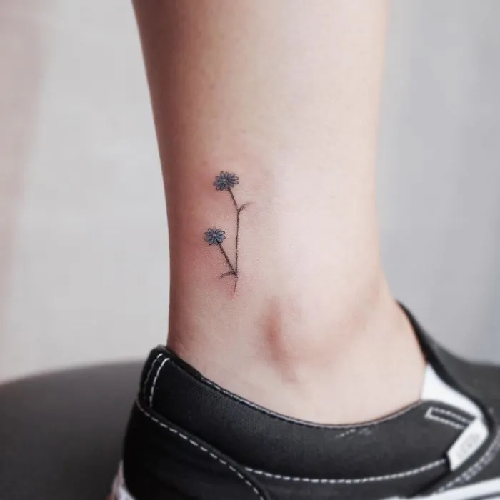 Minimalist tiny flower tattoo on ankle, embodying discreet tattoo design aesthetic.