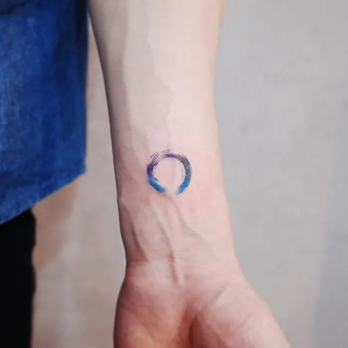 Minimalism tattoo featuring a small colorful circle on a forearm, showcasing discreet design style.