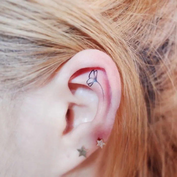Minimalism tattoo of a small butterfly inside an ear, highlighting discreet design.