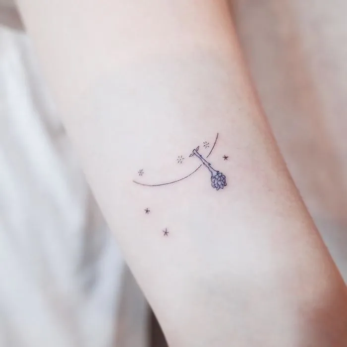 Minimalism tattoo of a hanging giraffe among stars on an arm.