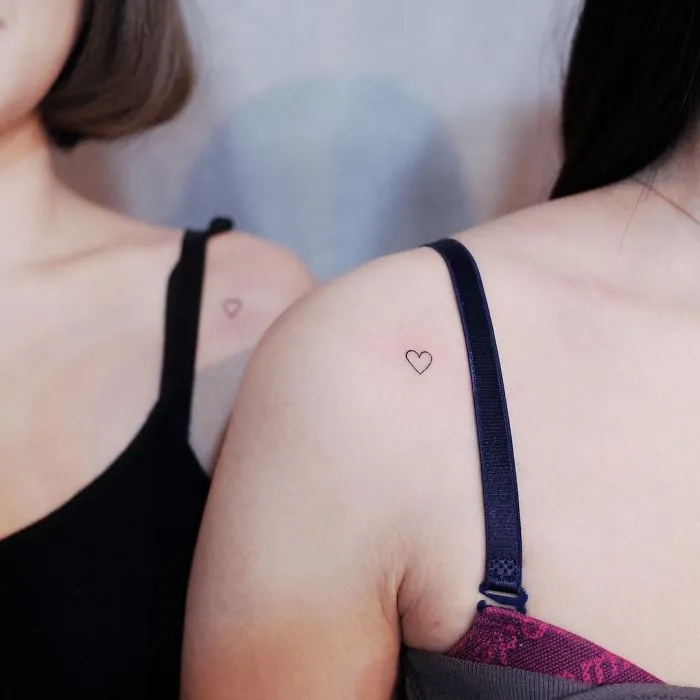 Minimalism tattoos featuring tiny heart designs on two women's shoulders, emphasizing discreet style.