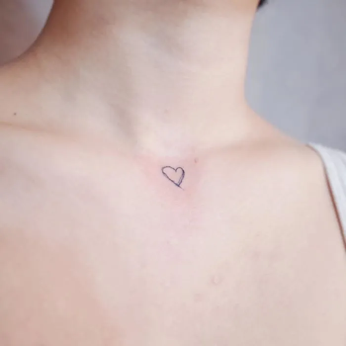Minimalism tattoo of a small heart on the upper chest.