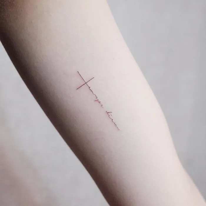 Minimalism tattoo on arm, featuring a delicate cross and line design.