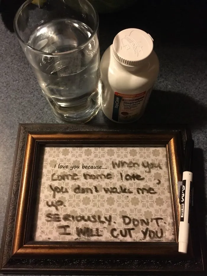 Framed funny marriage note with ibuprofen and glass of water on table.