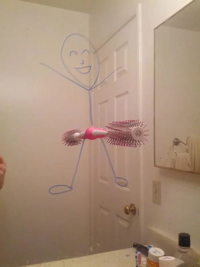 Stick figure drawn on a bathroom mirror with a brush as the body, humorously depicting marriage creativity.