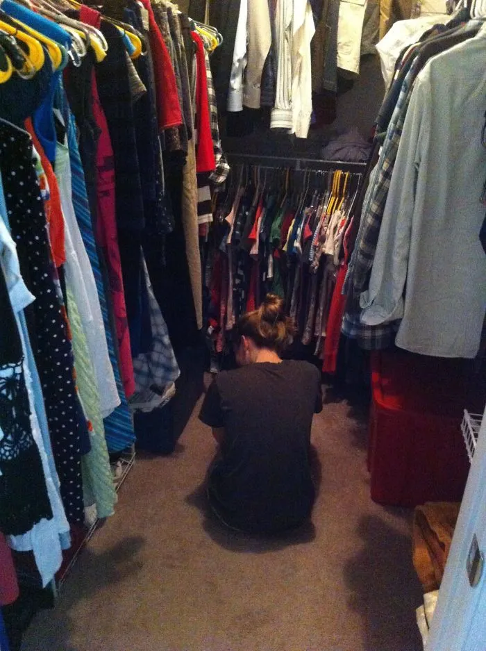 Person sitting on a closet floor surrounded by clothes, illustrating a funny moment in married life.