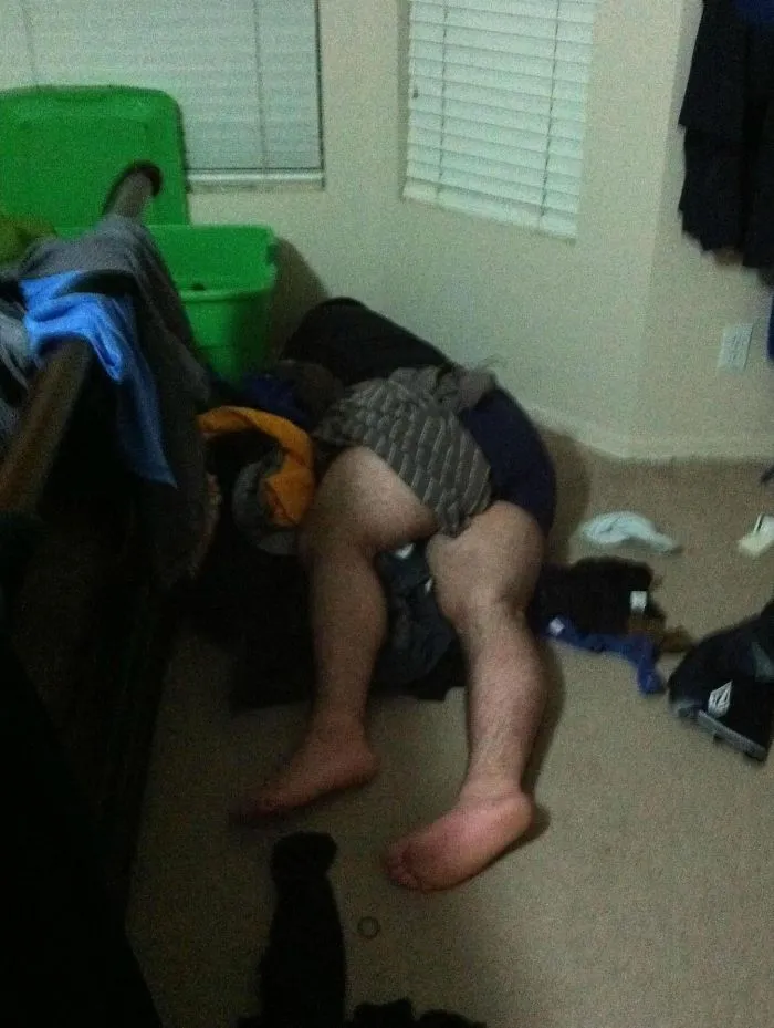 Man humorously asleep on a pile of clothes in a messy room, embodying funny aspects of married life.