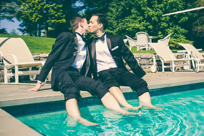 Two men kissing while near a pool 