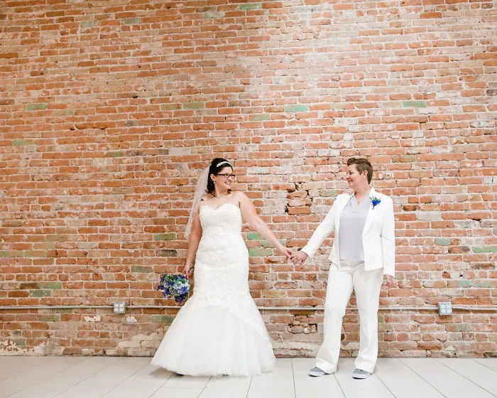 Two women holding hands near a brick wall 