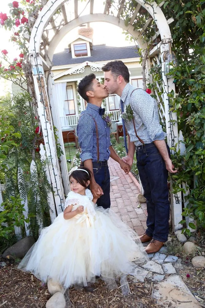 Two men kissing and holding hands with a small girl 