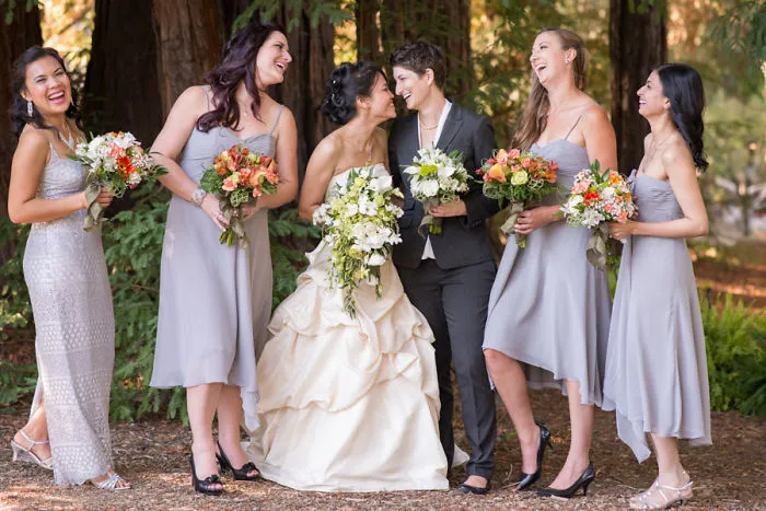 Tw women laughing and holding hands while grooms stand near by 