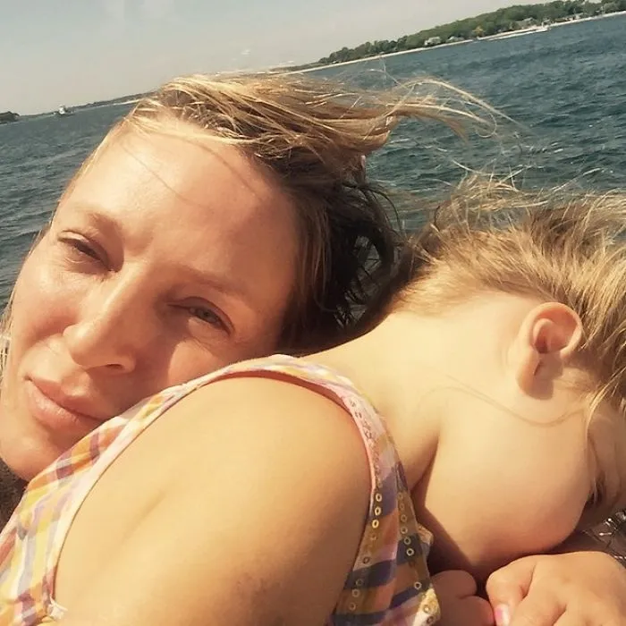 Celebrity without makeup, relaxing outdoors with a child, near a body of water.