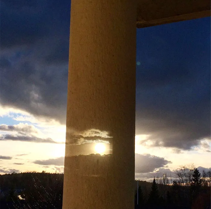 Image Reflected From Double Glazing Window Is Aligned With A Real Image Of Sun And Clouds Behind The Pillar