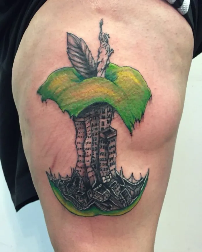 Tattoo of architectural buildings in an apple core design, featuring the Statue of Liberty and urban elements.