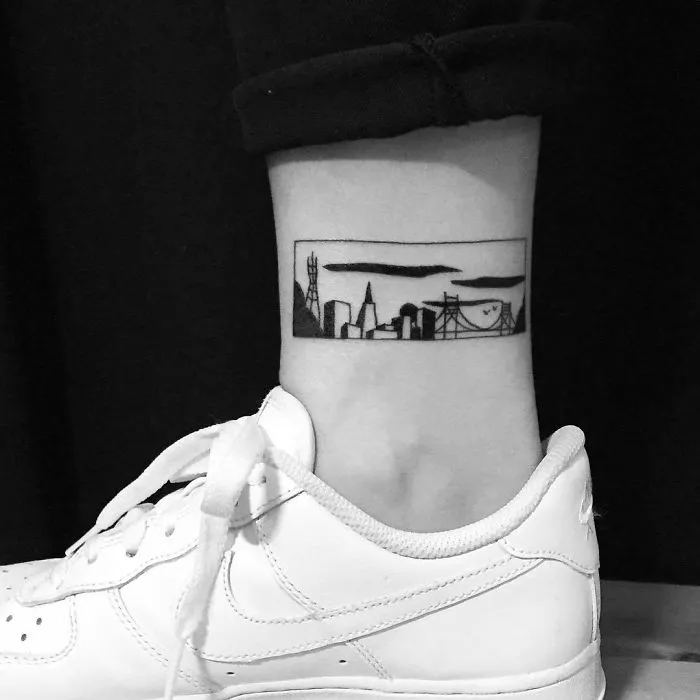 Minimalist architecture tattoo on ankle, featuring a city skyline in black ink.