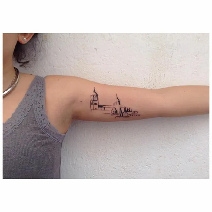Arm tattoo with architectural skyline design on a person wearing a gray tank top.